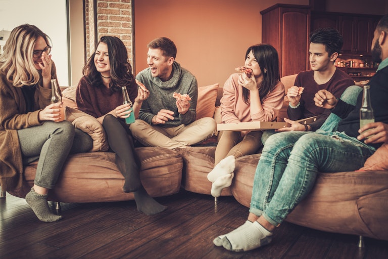 Group of young friends eating pizza in home interior