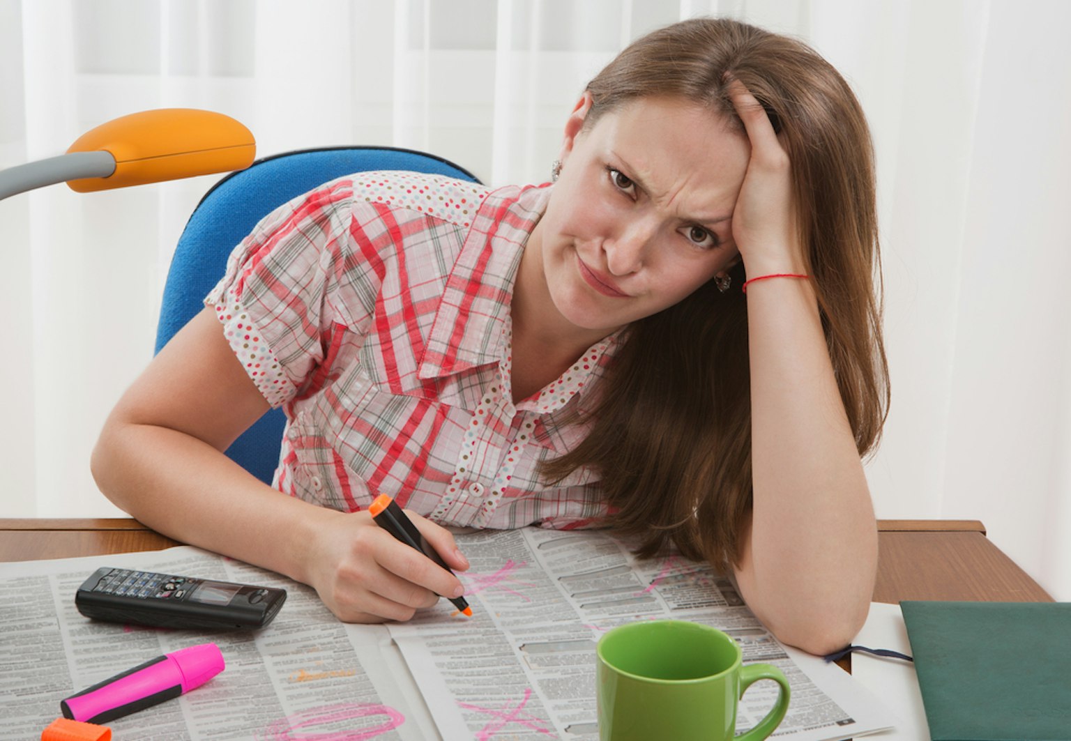 Woman writing on newspaper while looking upset