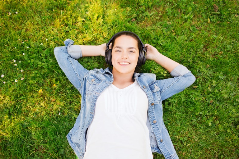 smiling young girl wearing headphones lying on grass